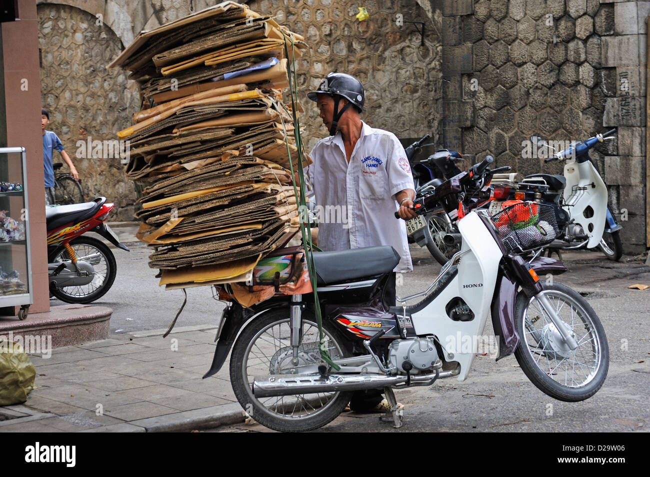 Vietnam street, Hanoi - Man carrying cardboard on the back of his scooter; people working Stock Photo