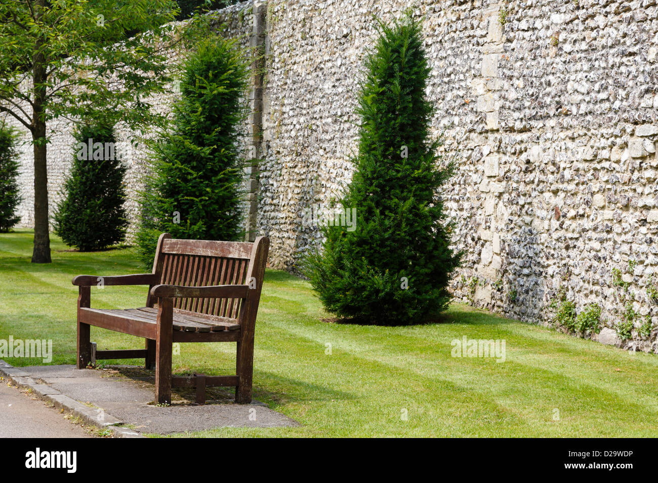 Wooden bench in a formal garden next to an ancient Roman wall in Winchester, UK Stock Photo