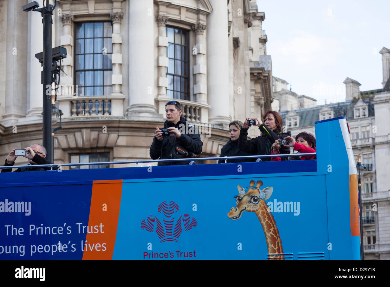 Tourists on the upper deck of an open double decker tourist bus take photographs as they travel through London. Stock Photo