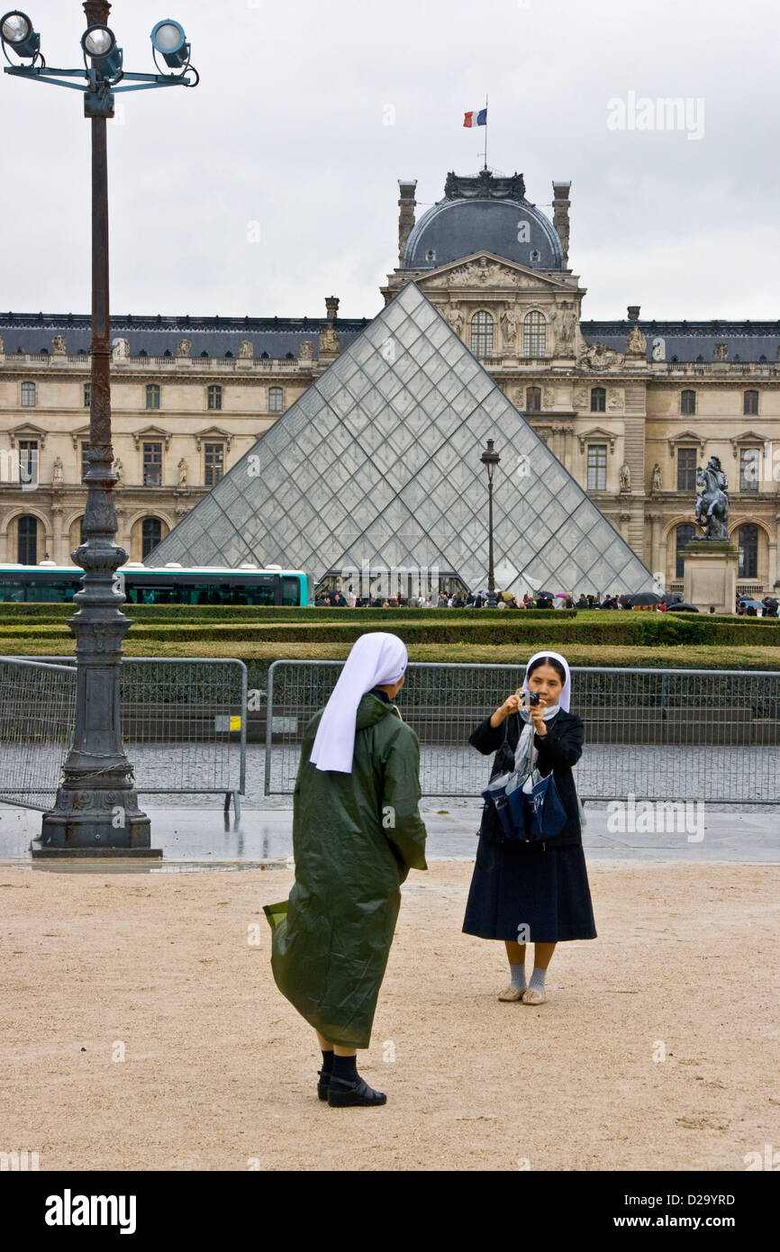 Two nuns taking a photograph with Louvre Pyramid by Leoh Ming Pei in background Paris France Europe Stock Photo