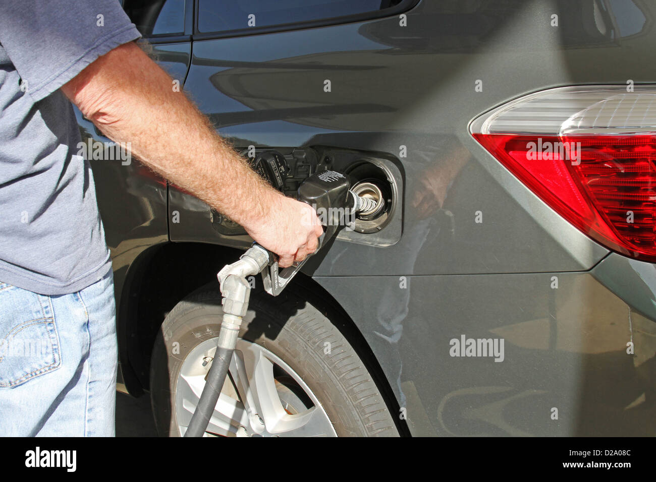 Man holding a nozzle at a gas pump filling the tank of his automobile