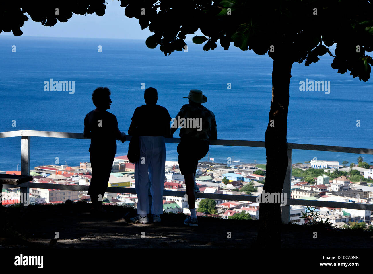 three tourists stand silhouetted, at the railing overlooking the Caribbean ocean and blue sky Stock Photo