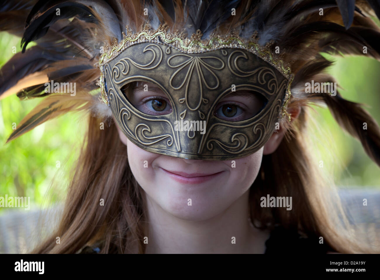Smiling girl wearing an elaborate feathered mask Stock Photo