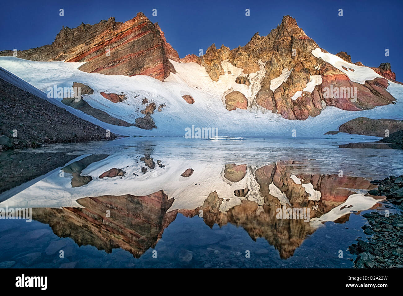 Central Oregon's Broken Top bathed in civil twilight reveals this icy reflection into Bend Glacier Lake. Stock Photo