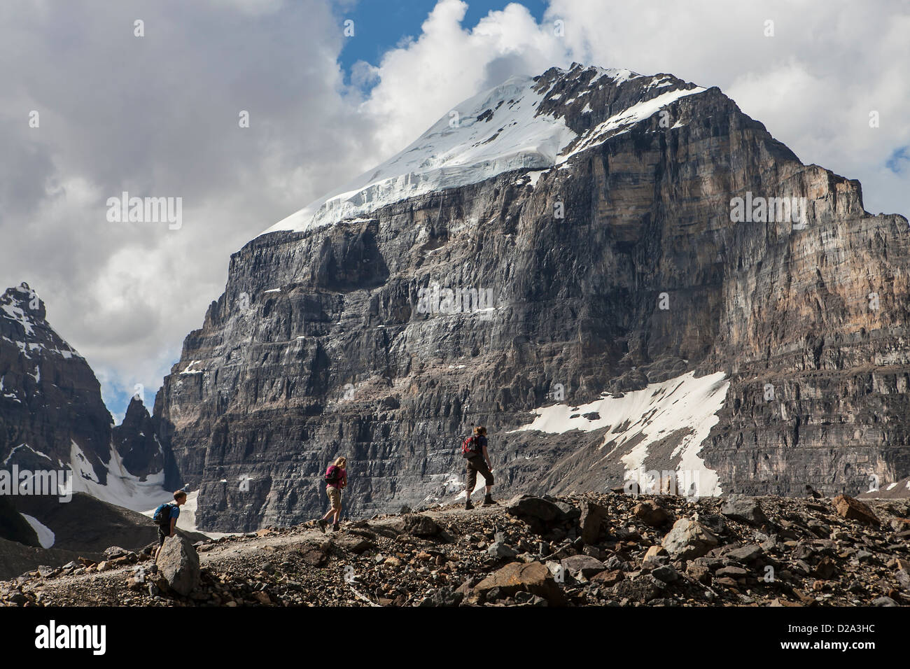 Hikers trek the Plain of Six Glaciers trail below the imposing face of Mount Victoria near Lake Louise, Banff National Park Stock Photo