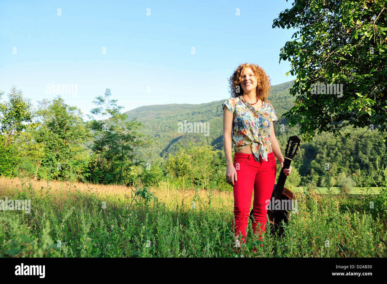 Woman holding guitar in grassy field Stock Photo