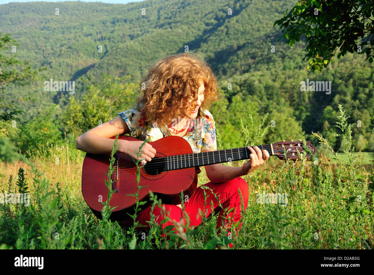Woman playing guitar in grassy field Stock Photo