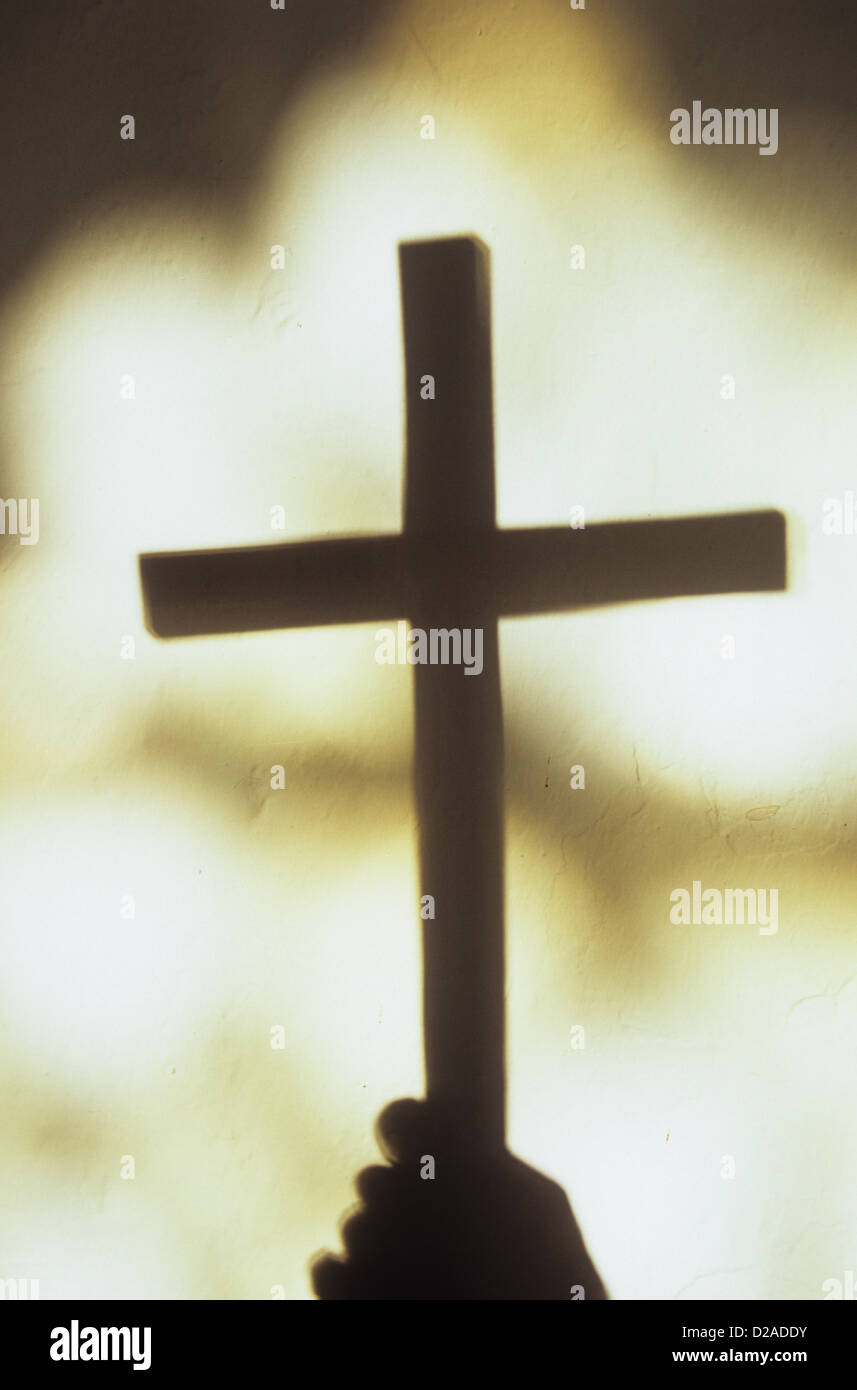 Shadow of hand holding large plain crucifix in front of blobs of light from church windows Stock Photo