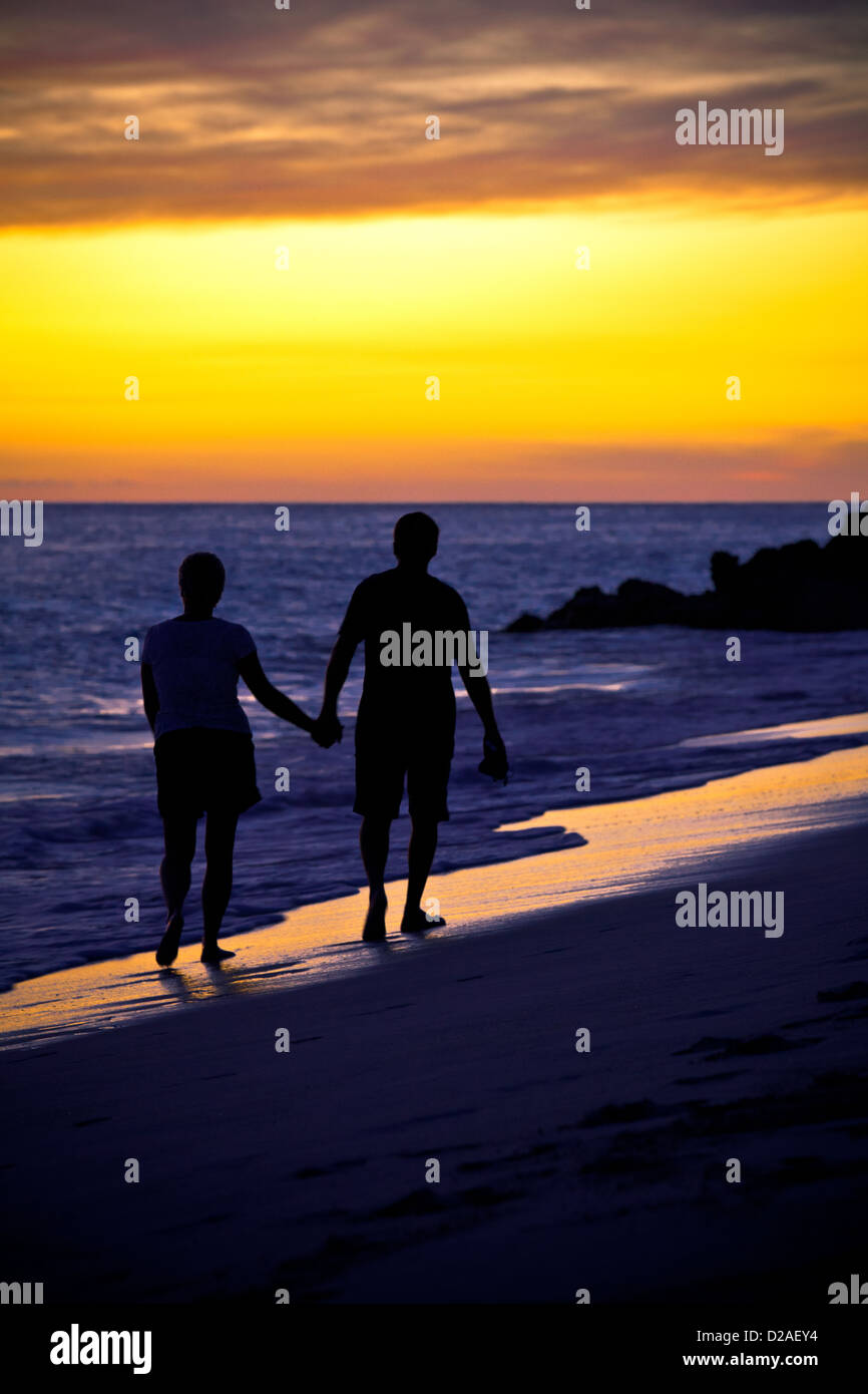 A silhouette of a couple holding hands, walking along the beach can be ...