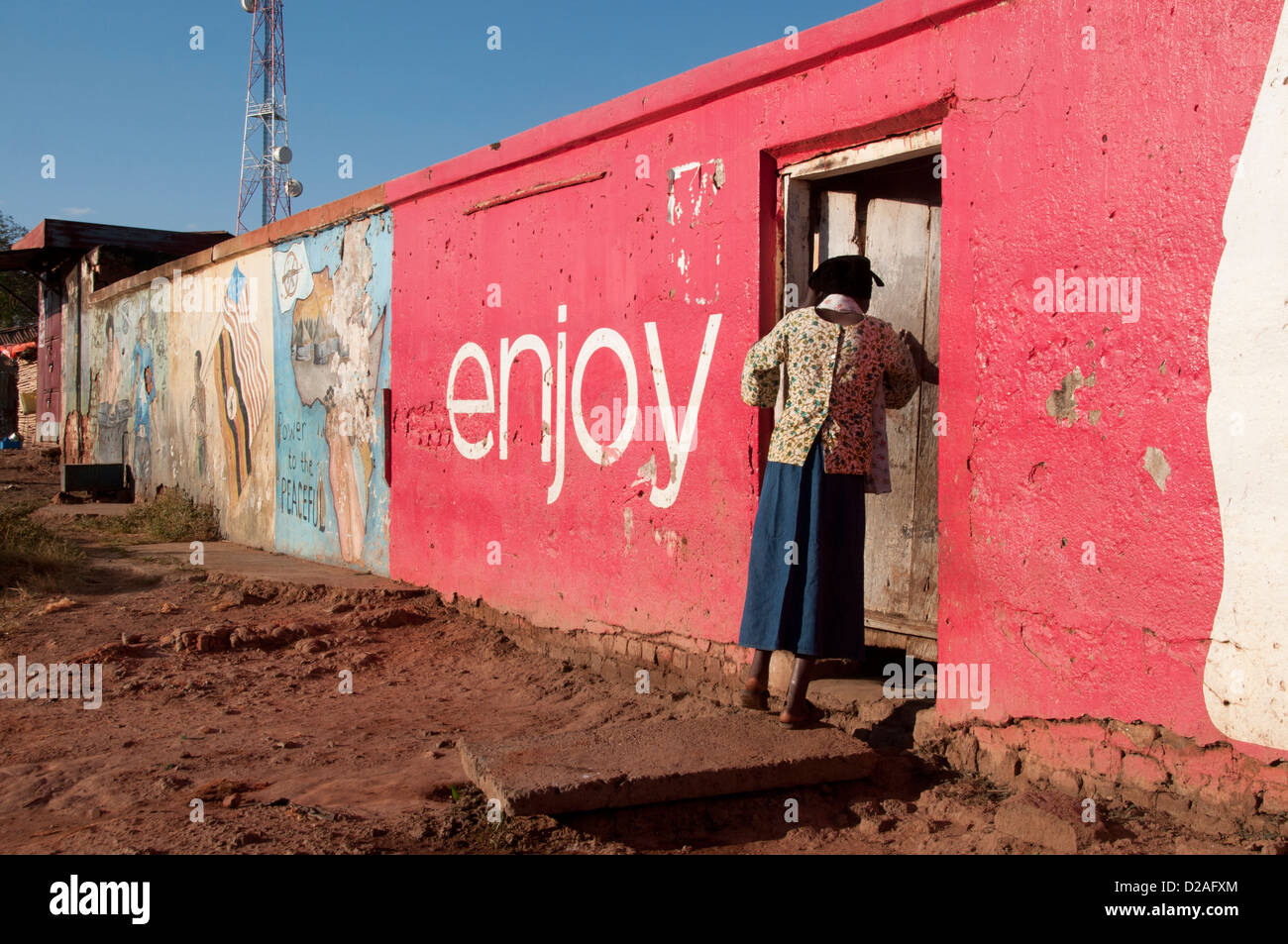 Uganda, Gulu. A woman goes into a door set in a red wall with Enjoy painted on it Stock Photo