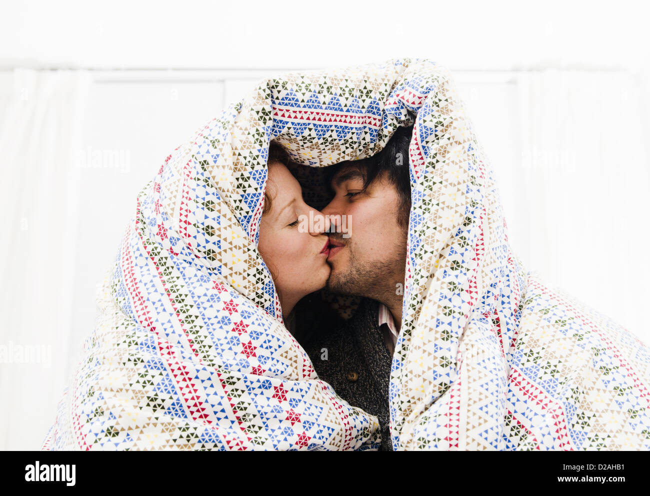 Couple kissing under duvet blanket Stock Photo