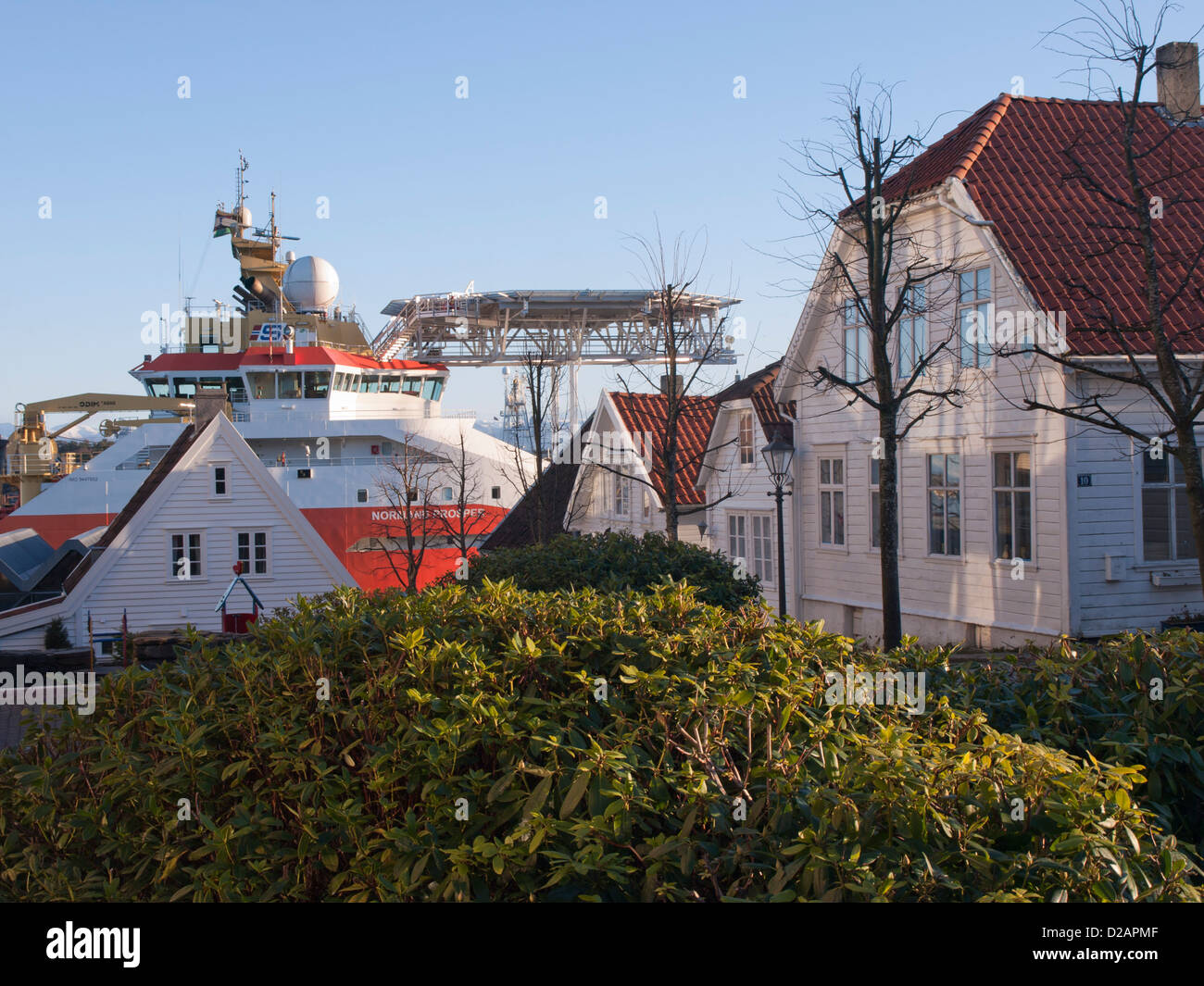 Rhododendron bushes and wooden houses in Old Stavanger  Norway. Harbour with oil industry supply ship can be seen below Stock Photo