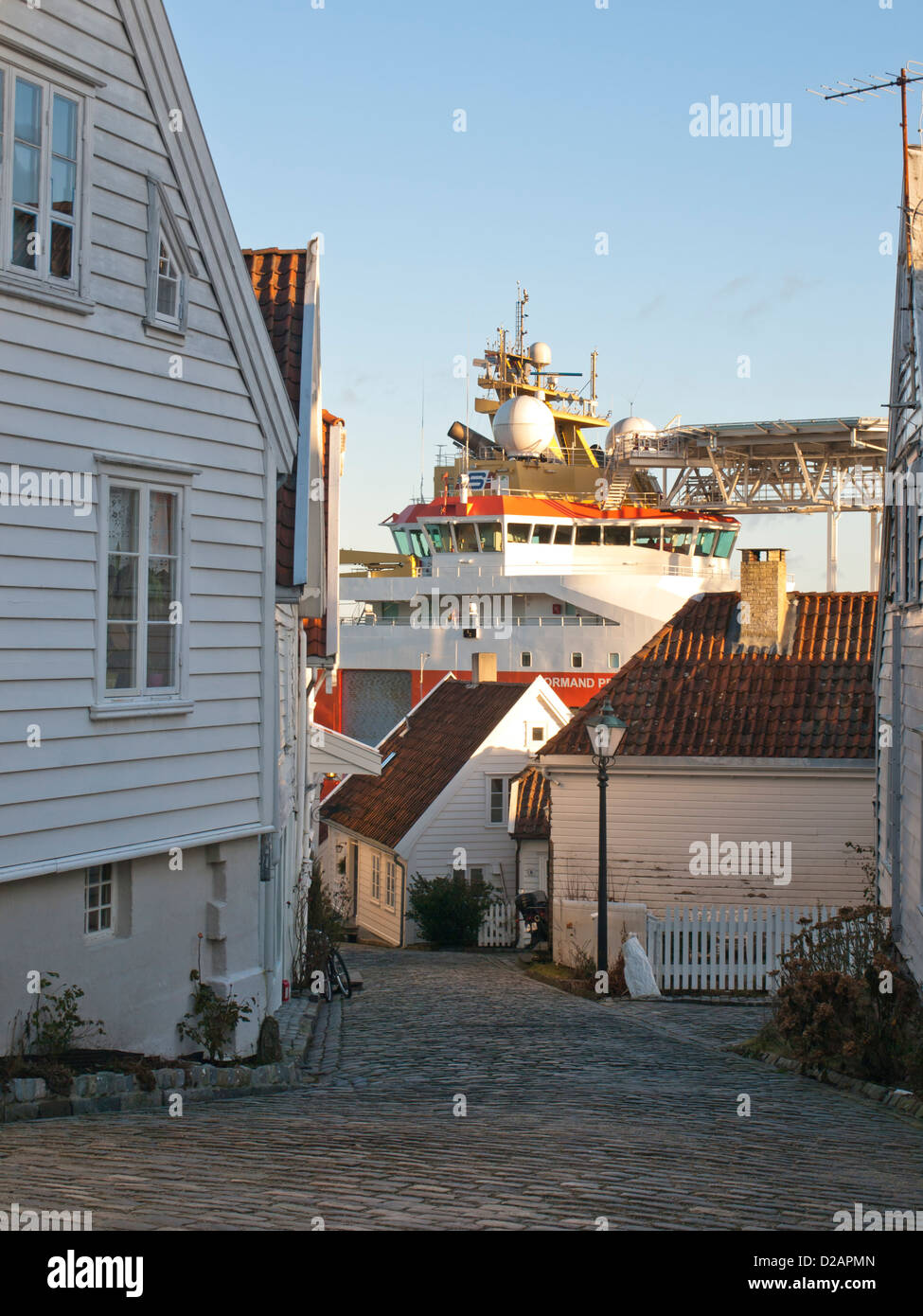 Steep cobbled street and wooden houses in Old Stavanger Norway. Sightseeing destination for cruise ships. Harbour with supply ship can be seen below Stock Photo