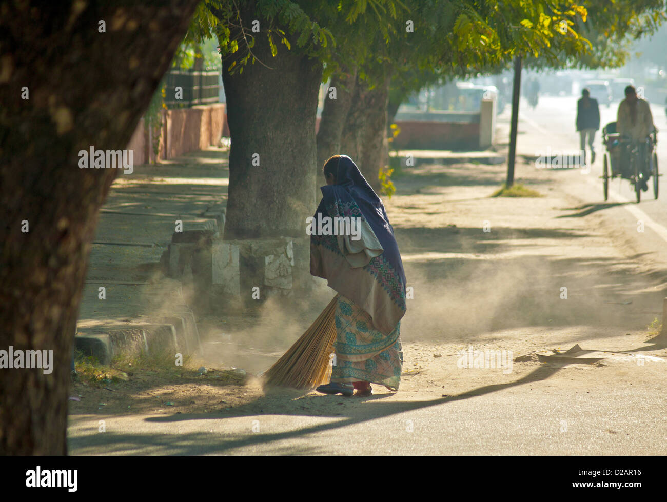 DUST FROM THE SWEEPERS BROOM AS SHE CLEARS THE DEBRIS FROM THE PAVEMENT JAIPUR RAJASTHAN INDIA Stock Photo