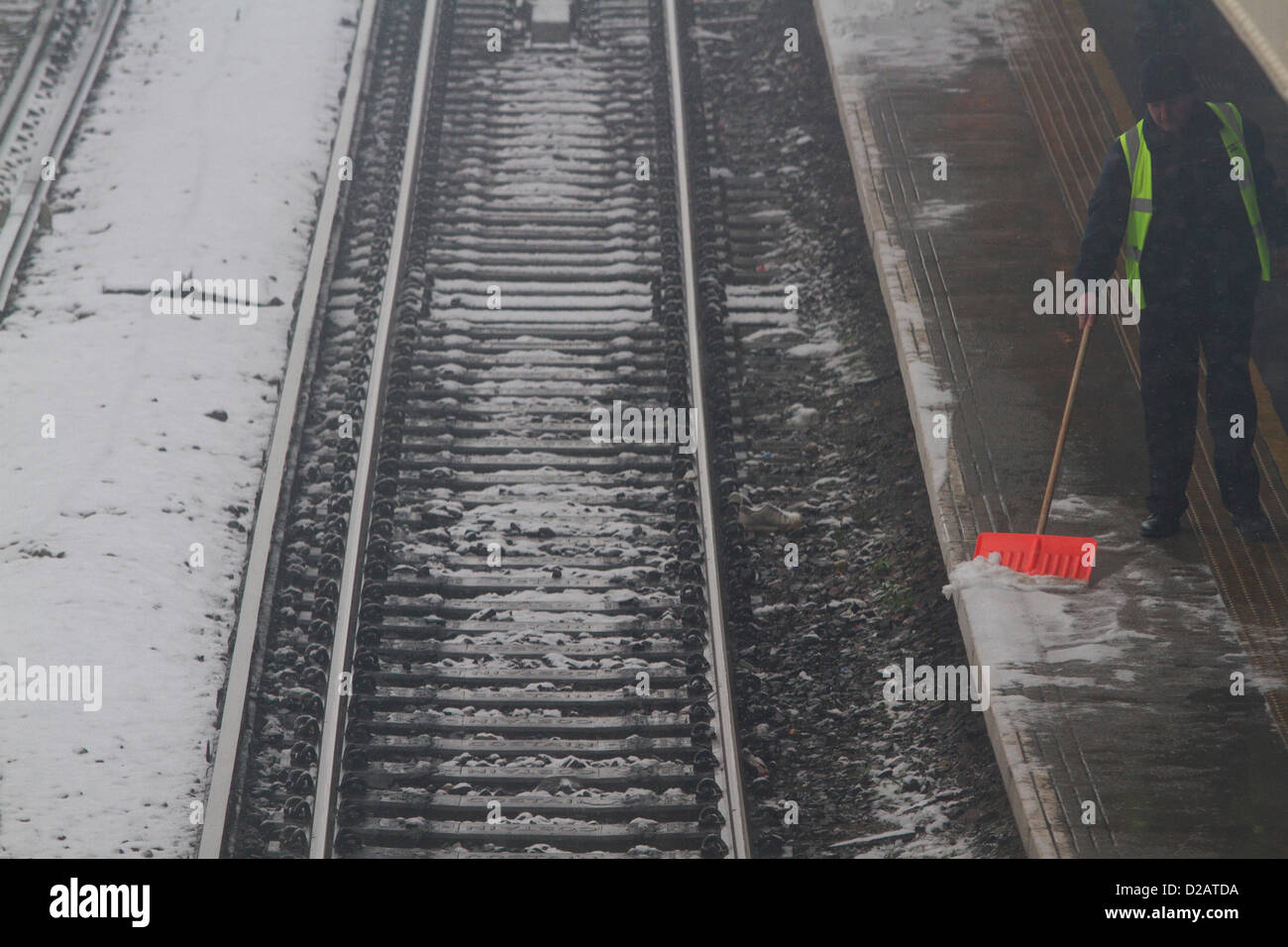 18th January 2013. London UK. A man sweeps the snow from a train station platform on to the track as Heavy snow falls on London and other parts of the UK causing travel disruption to air rail and train services and for commuters as the friday  rush  hour begins. Stock Photo