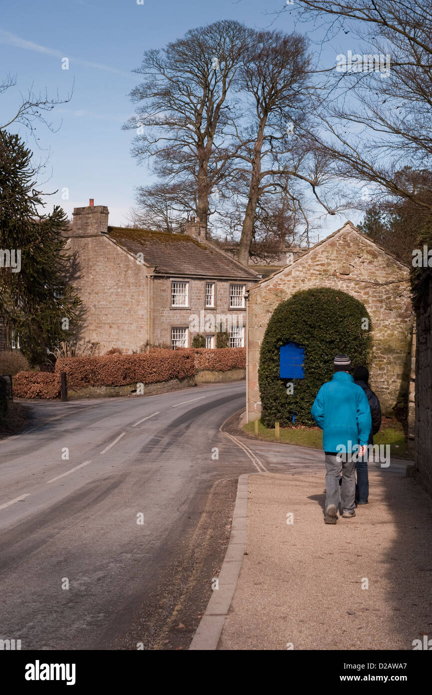 Rear view of couple on country walk, walking on roadside pavement, through quiet rural scenic village - Bolton Abbey, North Yorkshire, England, UK. Stock Photo