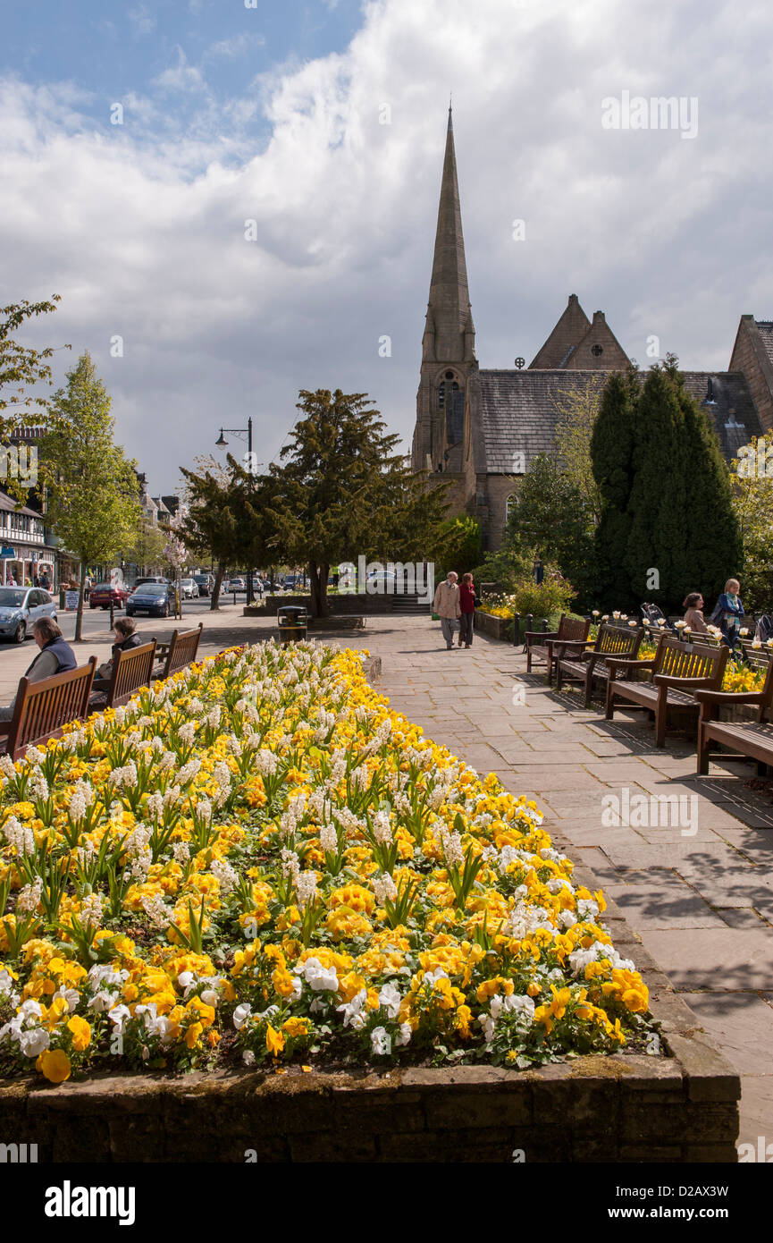 People relax by bright colourful spring flowers blooming in flowerbeds on sunny high street in scenic town - The Grove, Ilkley, Yorkshire, England, UK Stock Photo