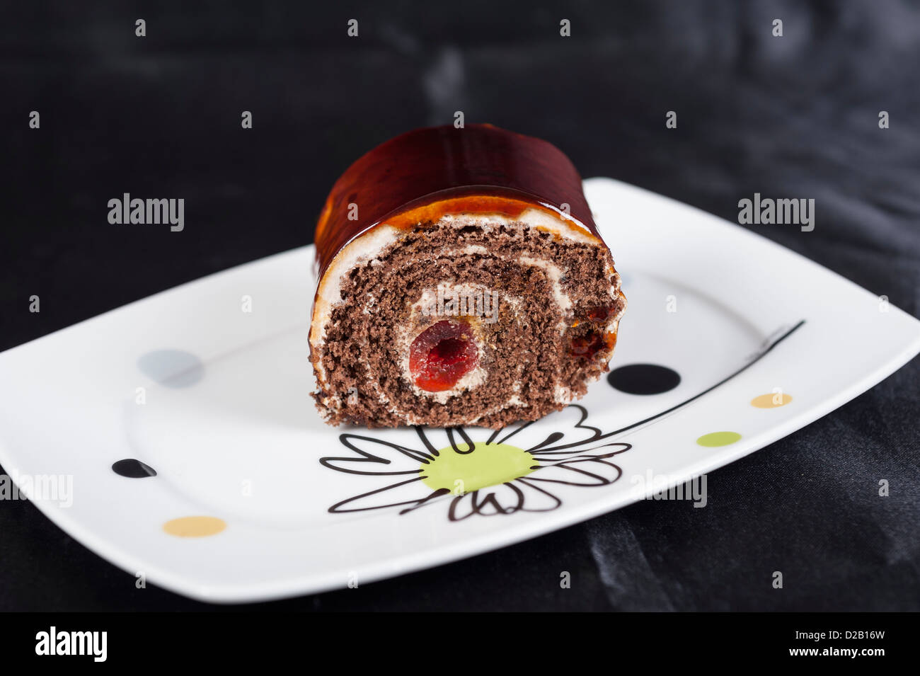 Chocolate sponge roll dessert with cherry on a white plate Stock Photo