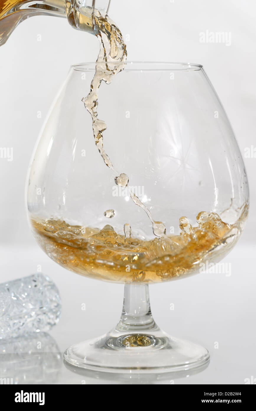 High speed photo of liquor pouring into a brandy snifter on white