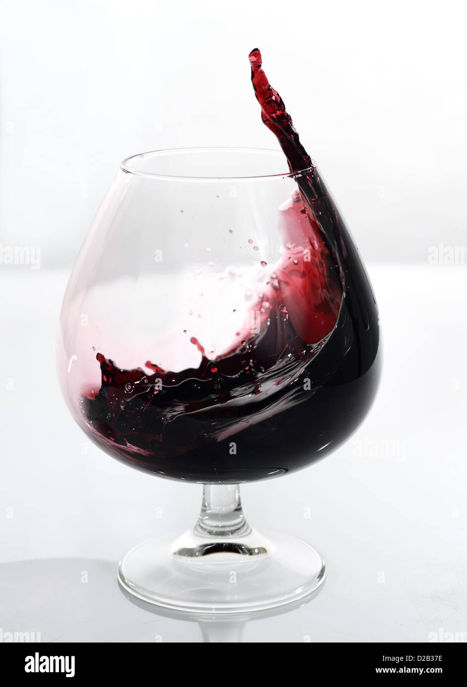Swirling and splashing port frozen motion in a glass snifter on white background Stock Photo