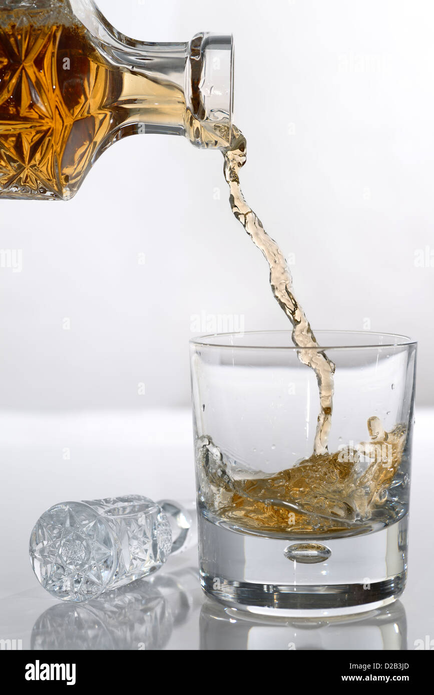 Pouring scotch from a crystal decanter into a whiskey tumbler glass on white background Stock Photo