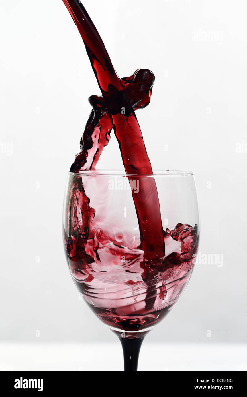 High speed stop motion exuberant frozen splash of red wine poured into glass stemware on a white background Stock Photo