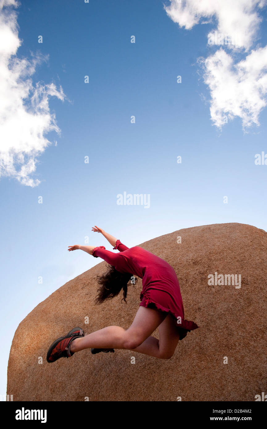 Female dancer in a red dress leaping up into an abstract sky-stone landscape. Stock Photo