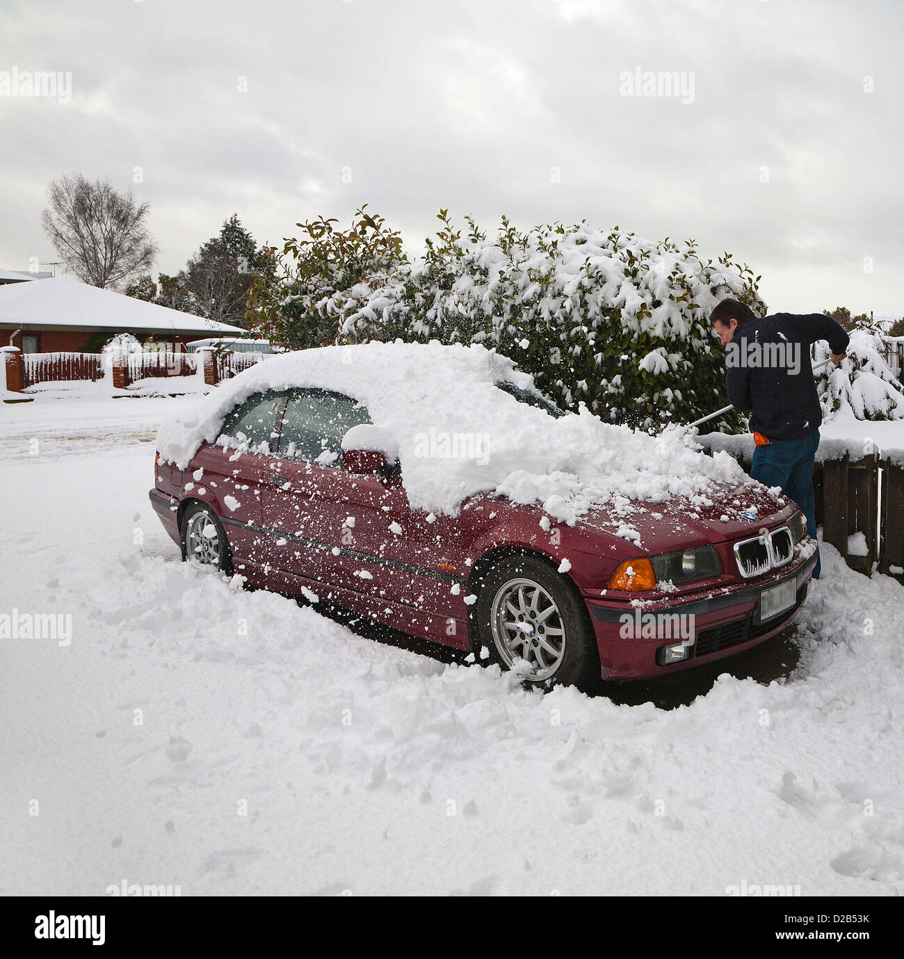 A man using a broom to brush deep snow off his car in the driveway