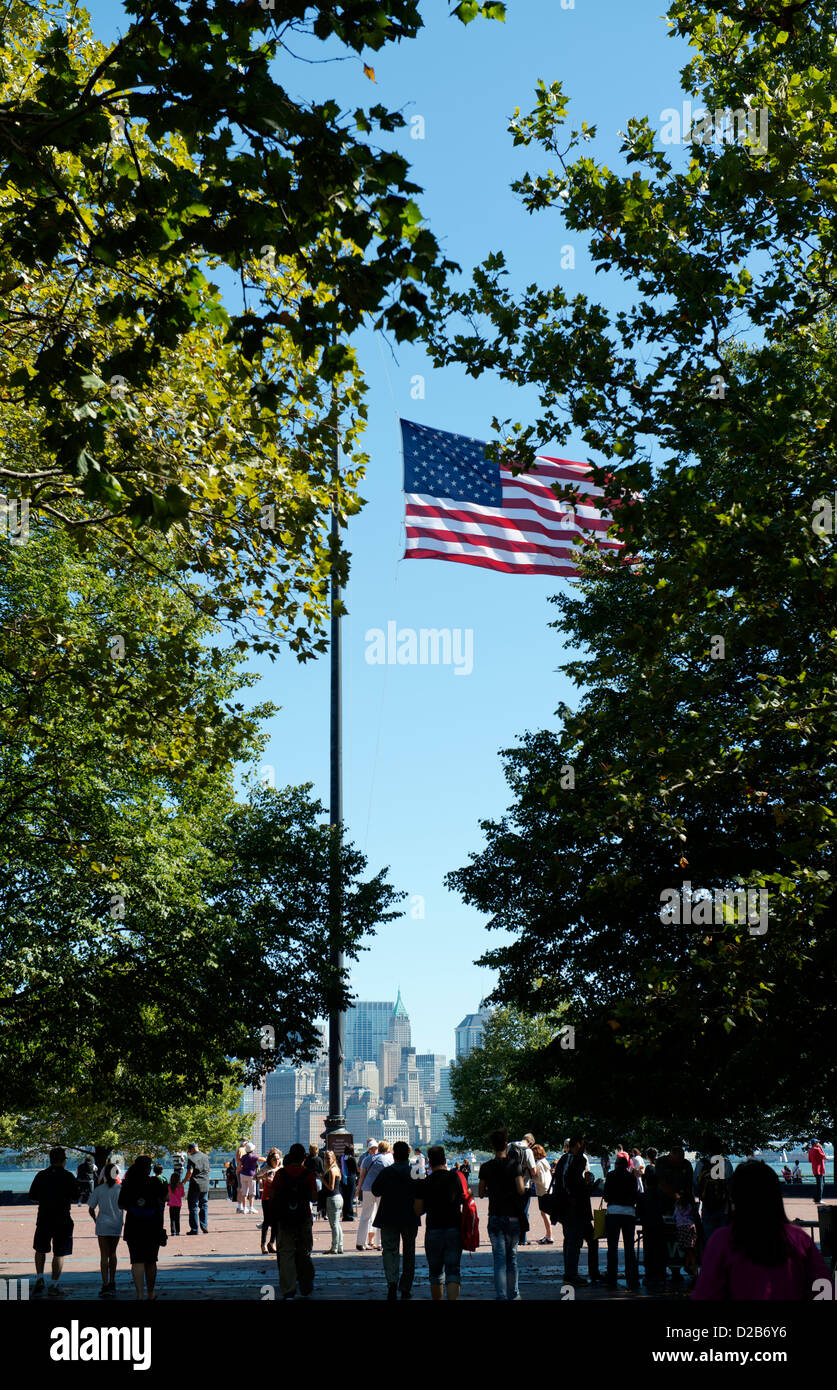 US flag seen between trees on Liberty Island with Lower Manhattan in the distance. Stock Photo