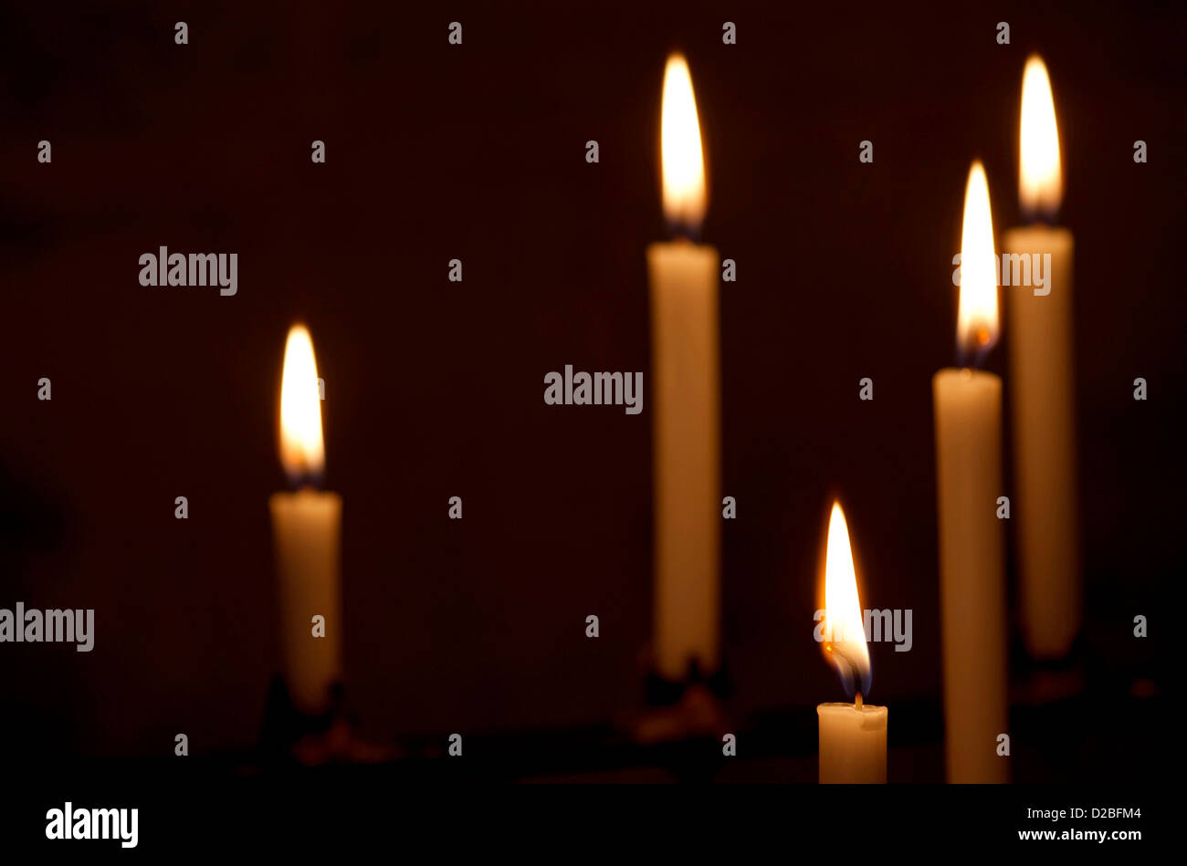 Closeup of five white prayer candles all lit, focus on nearest candle