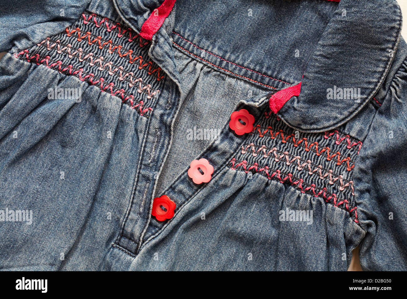 red and pink daisy flower shaped buttons and smocking on little girl's denim smock dress Stock Photo