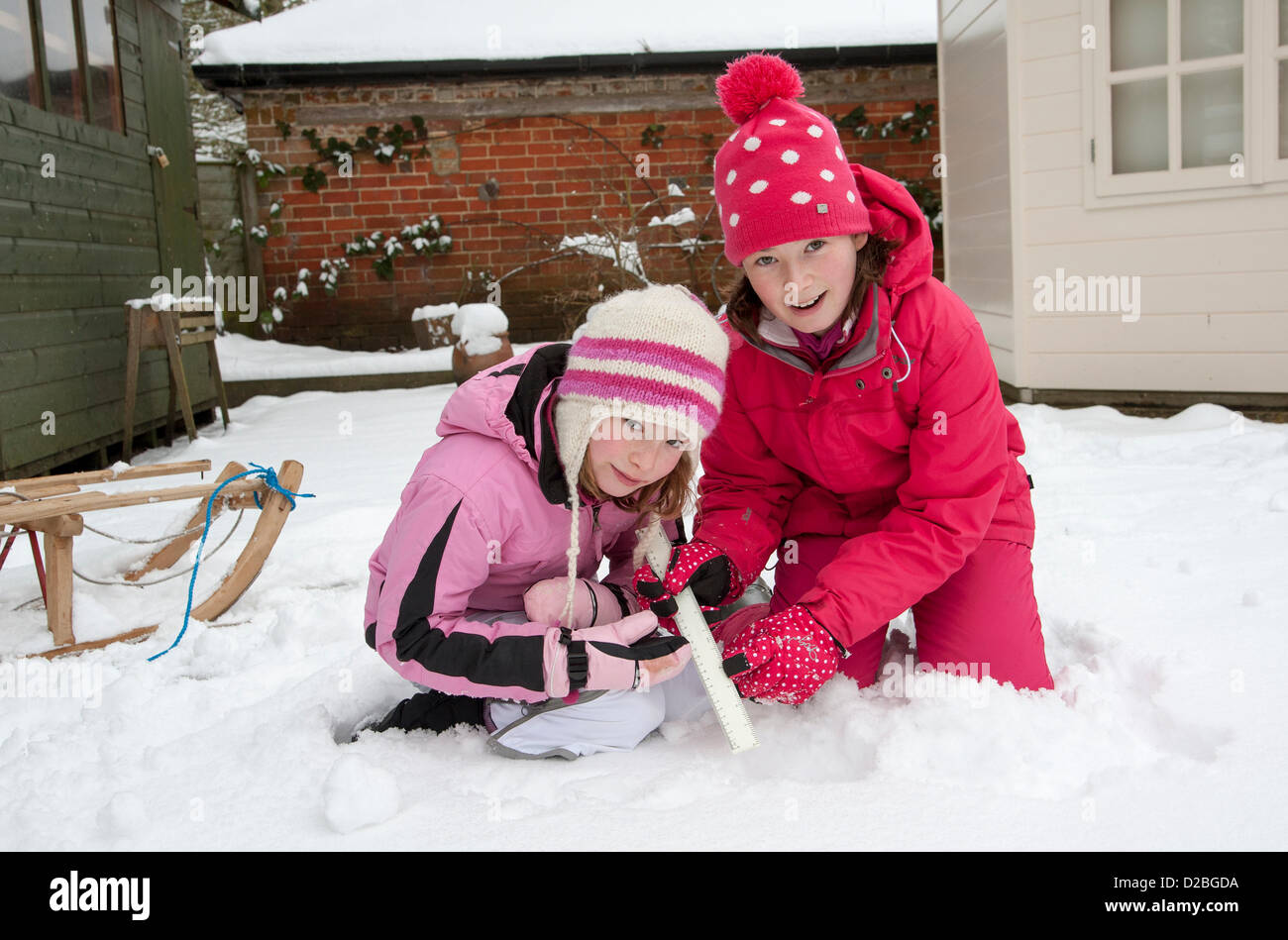 Winter snow in Hampshire and these young girls are seen using a ruler to measure the depth of the snow in a Hampshire garden Stock Photo