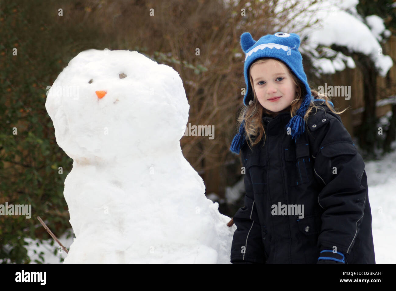 19/01/2013, Scarborough, England. 6 year old Eve Crowdy stands next to a snowman she just made in her garden with a big smile. Image is model released. Stock Photo