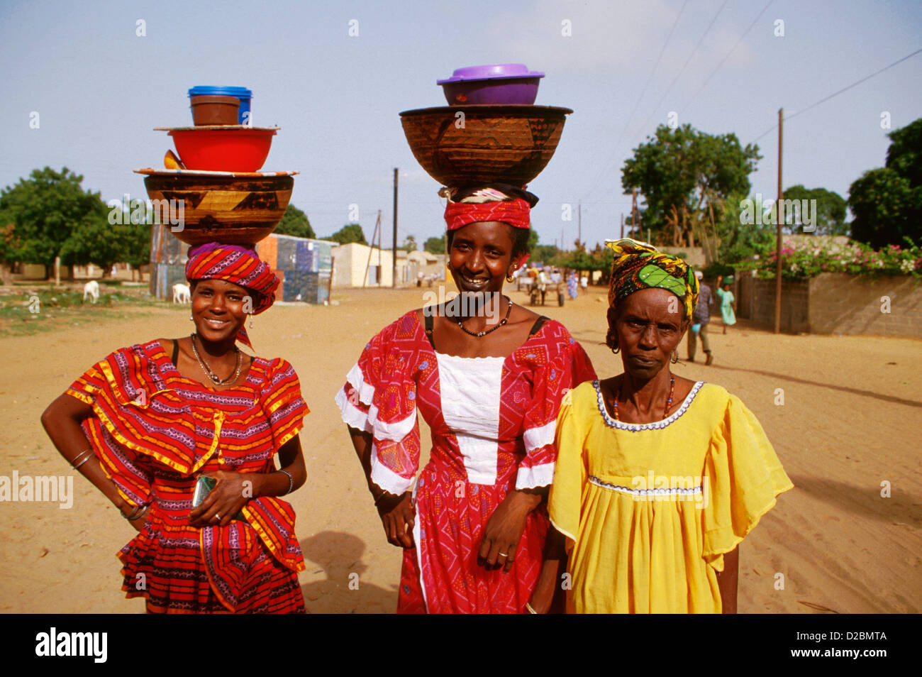 Senegal, M'Bour Region. Village Women In Traditional Colorful Dresses And  Bowls Balancing On Their Heads Stock Photo - Alamy