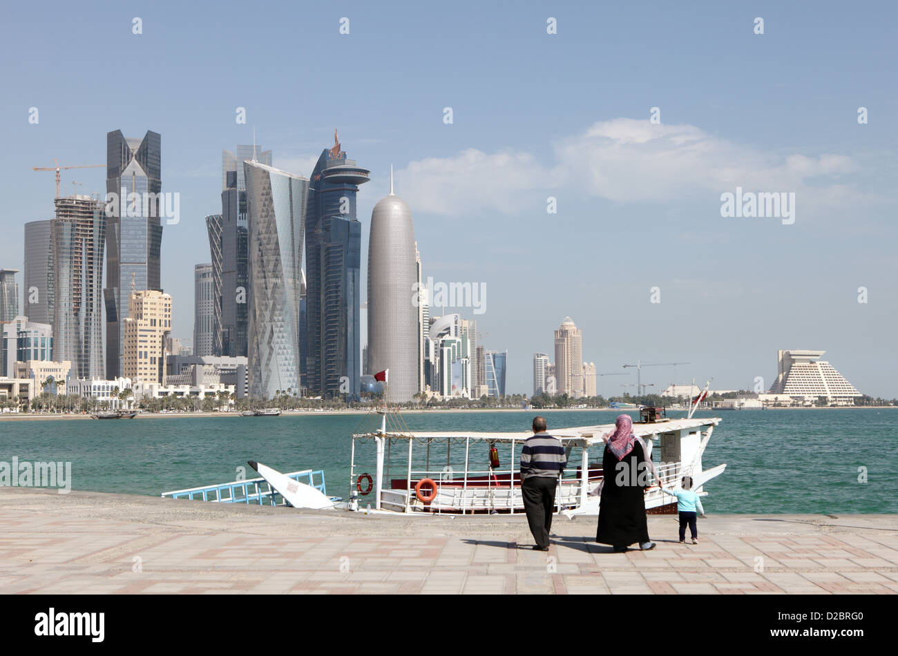 A Muslim family, three people, enjoy an outing on the Corniche, in Doha, Qatar, in the shadow of the  high-rise development Stock Photo