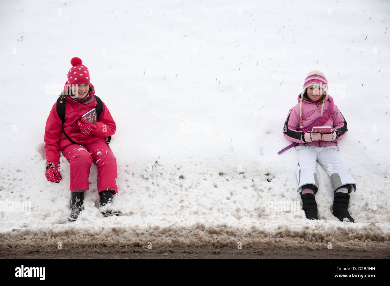 Young schoolgirls sitting on the roadside after a heavy fall of snow rural location in Hampshire England UK Stock Photo