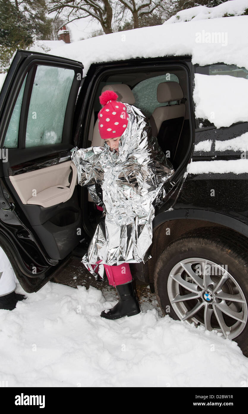 Young child keeping warm with a foil blanket wrapped around her. Car