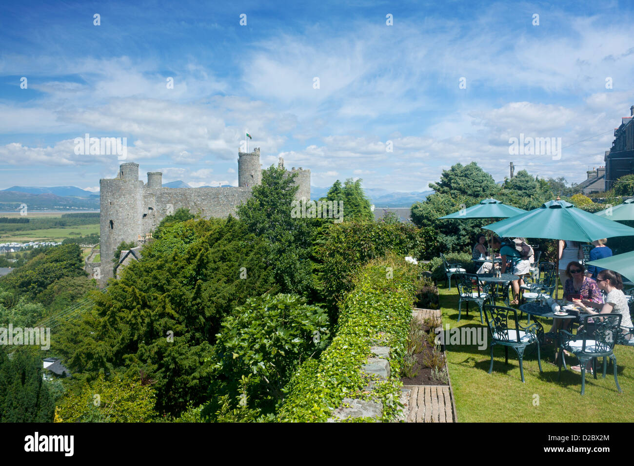 People enjoying lunch on the outdoor terrace at the Plas Cafe with Harlech Castle and Snowdonia in background Gwynedd Wales UK Stock Photo