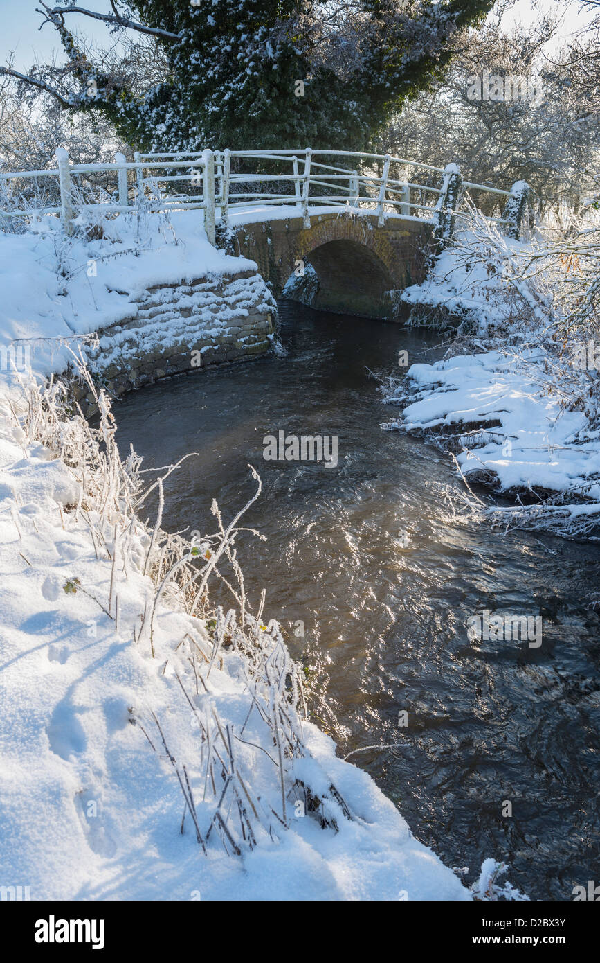 River Stiffkey flowing under brick footbridge in snowy landscape, Houghton St Giles, Norfolk, England, January Stock Photo