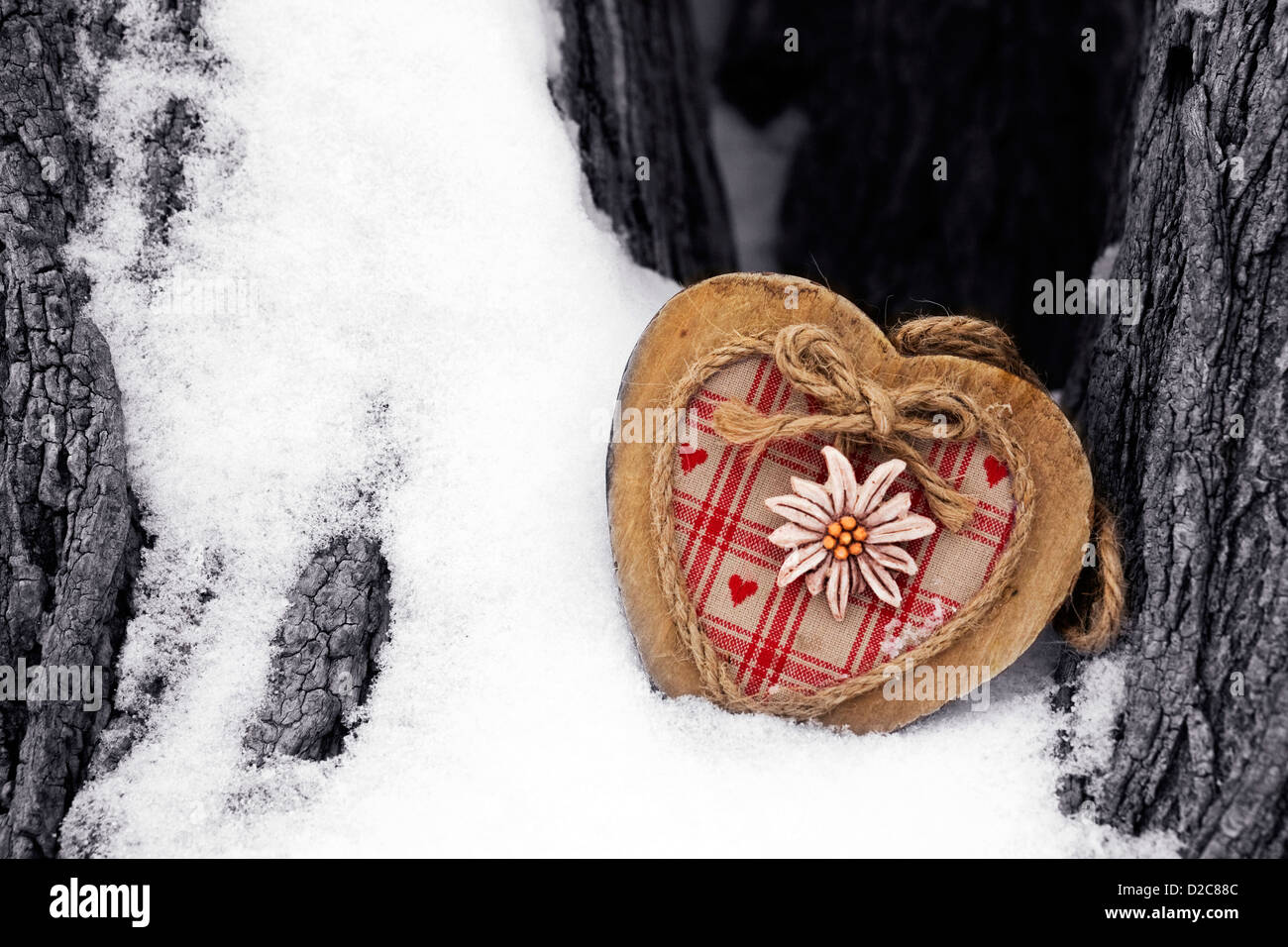 A decorative wooden heart nestled in a snowy tree trunk. Stock Photo