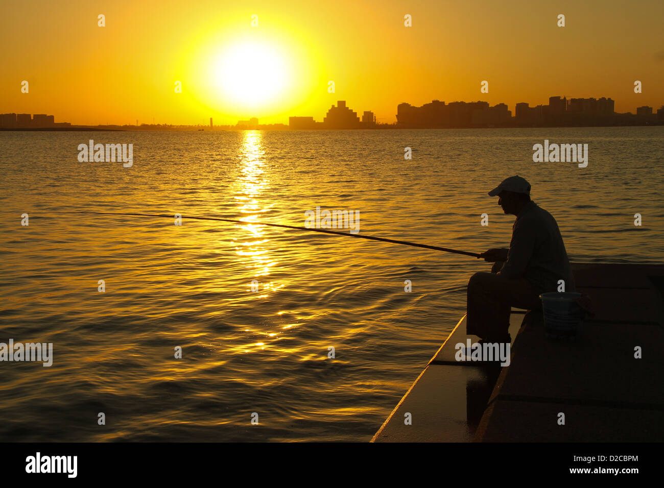 A man seen fishing a sunrise at Doha Bay Stock Photo