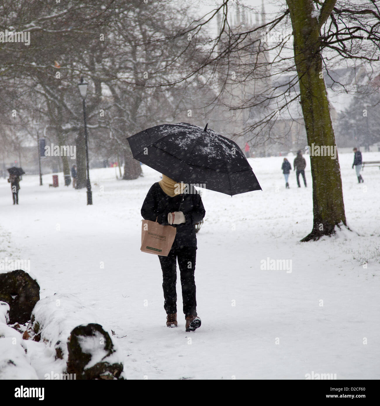 20 January 2013  13.10 PM - Snow falls on Clapham Common in Clapham, London, UK. Person with umbrella walks along path with Saint Michaels Church Behind Stock Photo