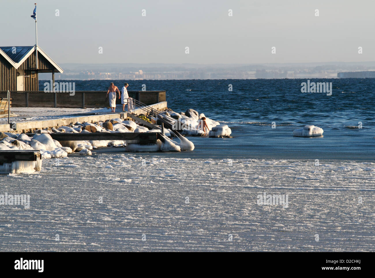 Winter swimmers jumping into the icy Sound at Rungsted harbour, Denmark.  Flag and warm club house to the left. Stock Photo
