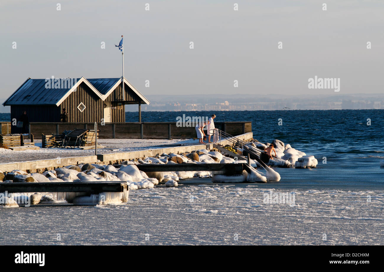Winter swimmers jumping into the icy Sound at Rungsted harbour, Denmark. Flag and warm club house to the left. Stock Photo