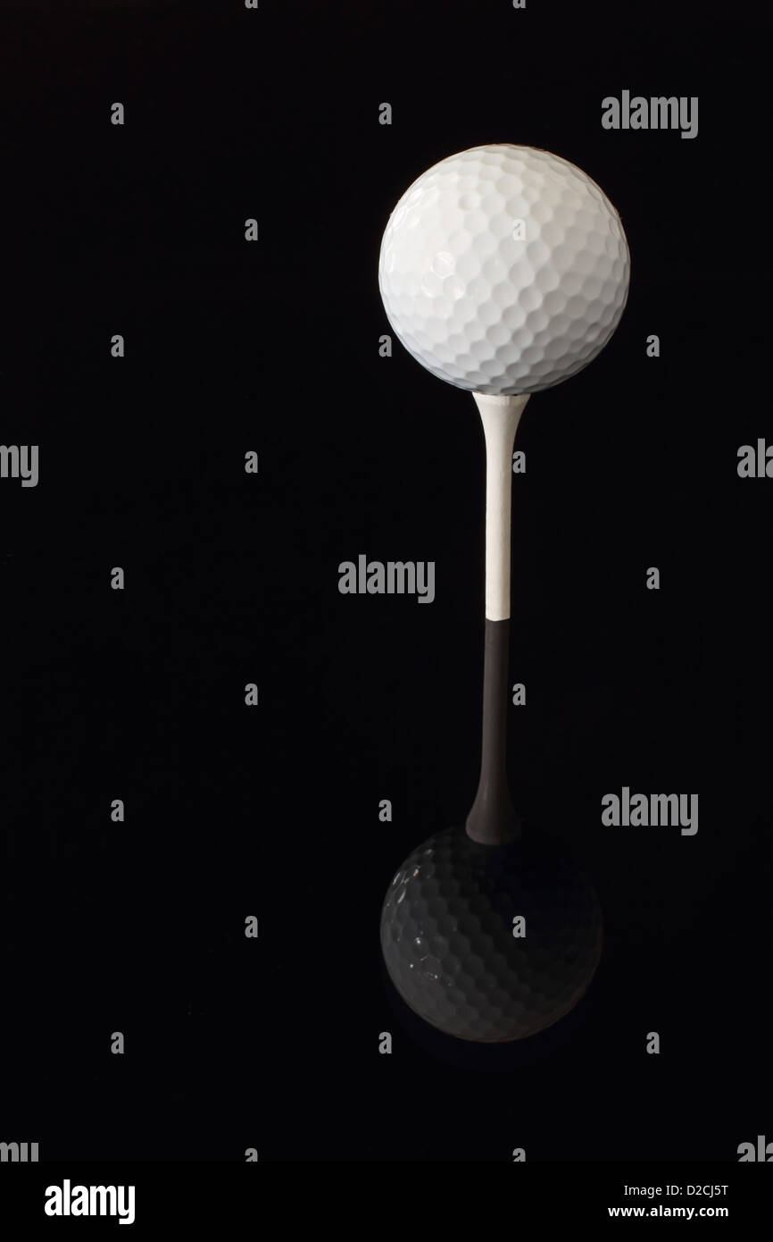 A golfball teed up on a white tee reflecting on a black surface. Stock Photo