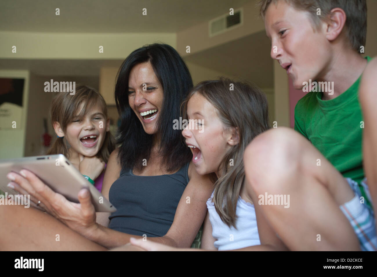 Mother and her three kids looking at an ipad tablet together and laughing at home. Stock Photo