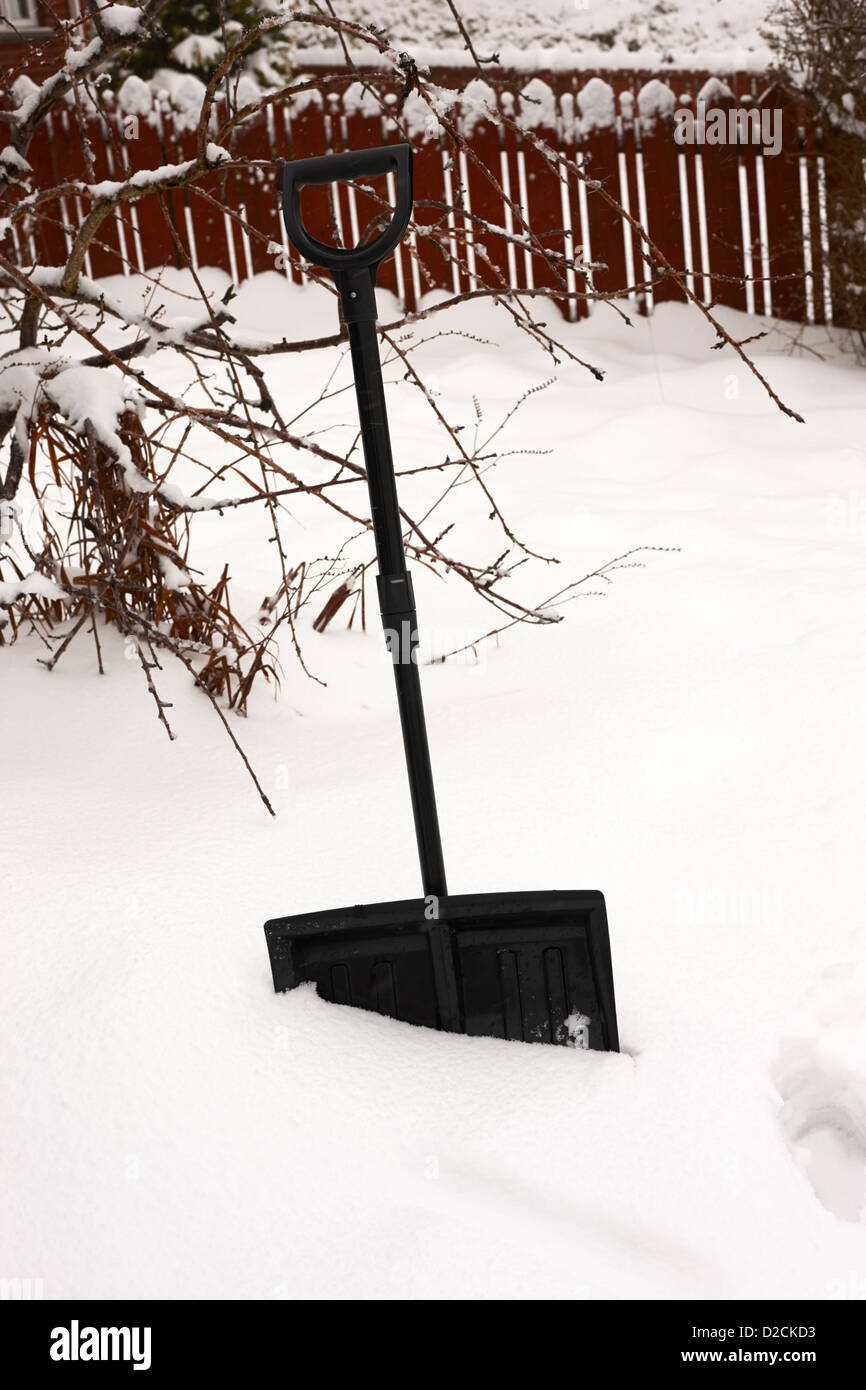 snow scoop shovel in deep snow in garden during bad winter weather
