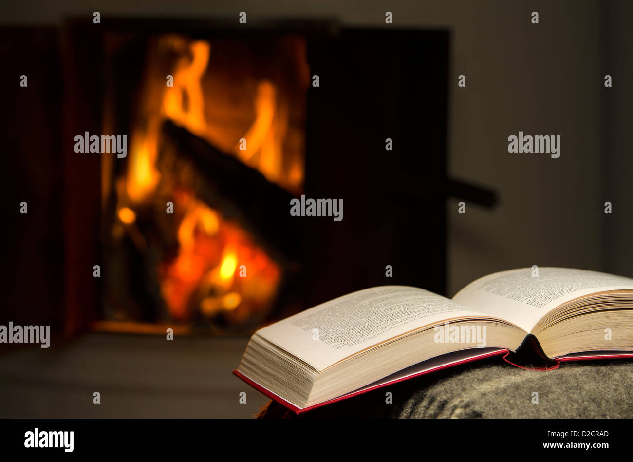 Peaceful image of open book resting on a arm rest of a couch. Warm fireplace on background. Stock Photo