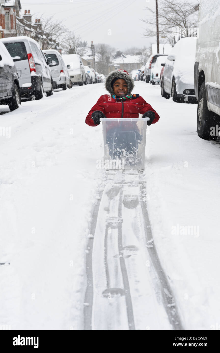 Young boy sitting in plastic container on snow, United Kingdom. Stock Photo