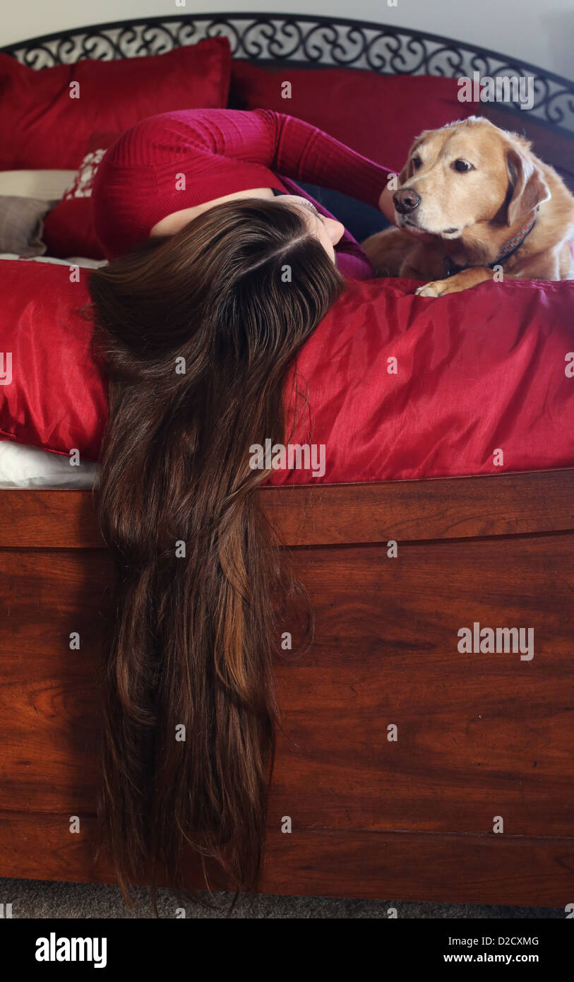A woman with long hair and a dog lying together on a bed. Stock Photo
